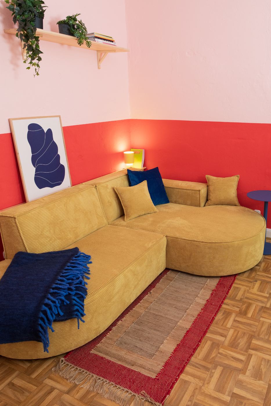 The Cast Area — cozy corner sofa in mustard corduroy, pink and red walls, framed art