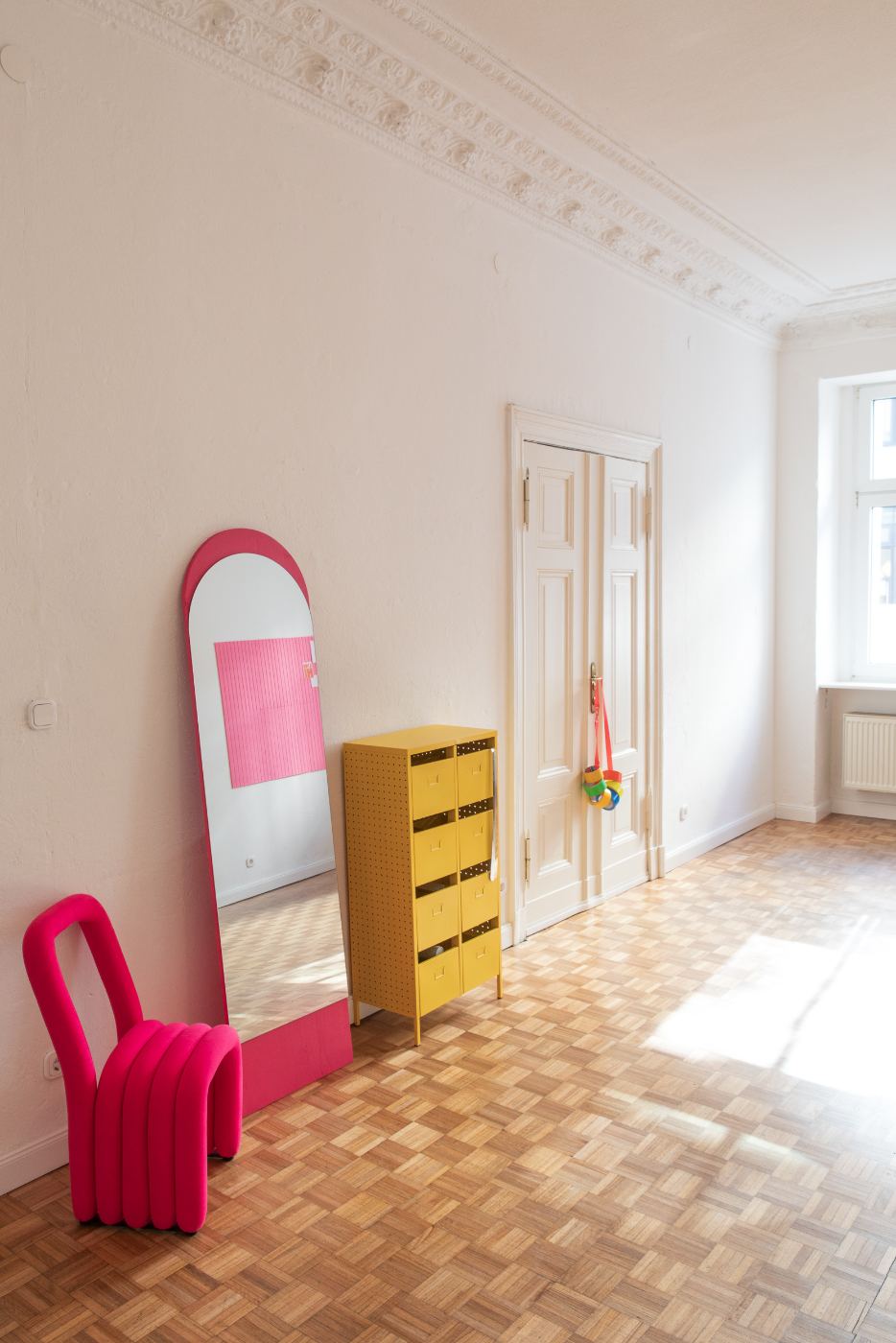 The Fitting Room — pink chair, arched mirror, yellow drawer cabinet on parquet floor