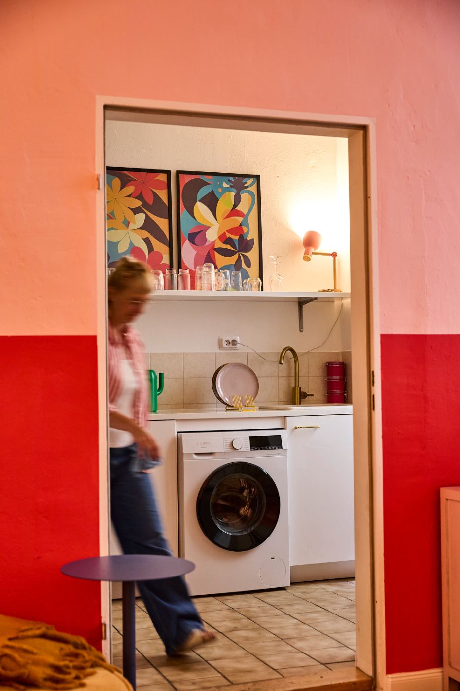 The Kitchen — coral and red walls, washing machine, colorful artwork