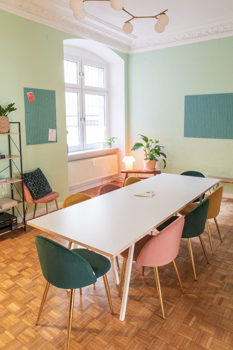 The Meeting Room — sage-green walls, multi-colored velvet chairs around a large white table, brass chandelier